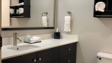 A modern bathroom with a white sink, dark cabinetry, a large mirror, and a toilet.