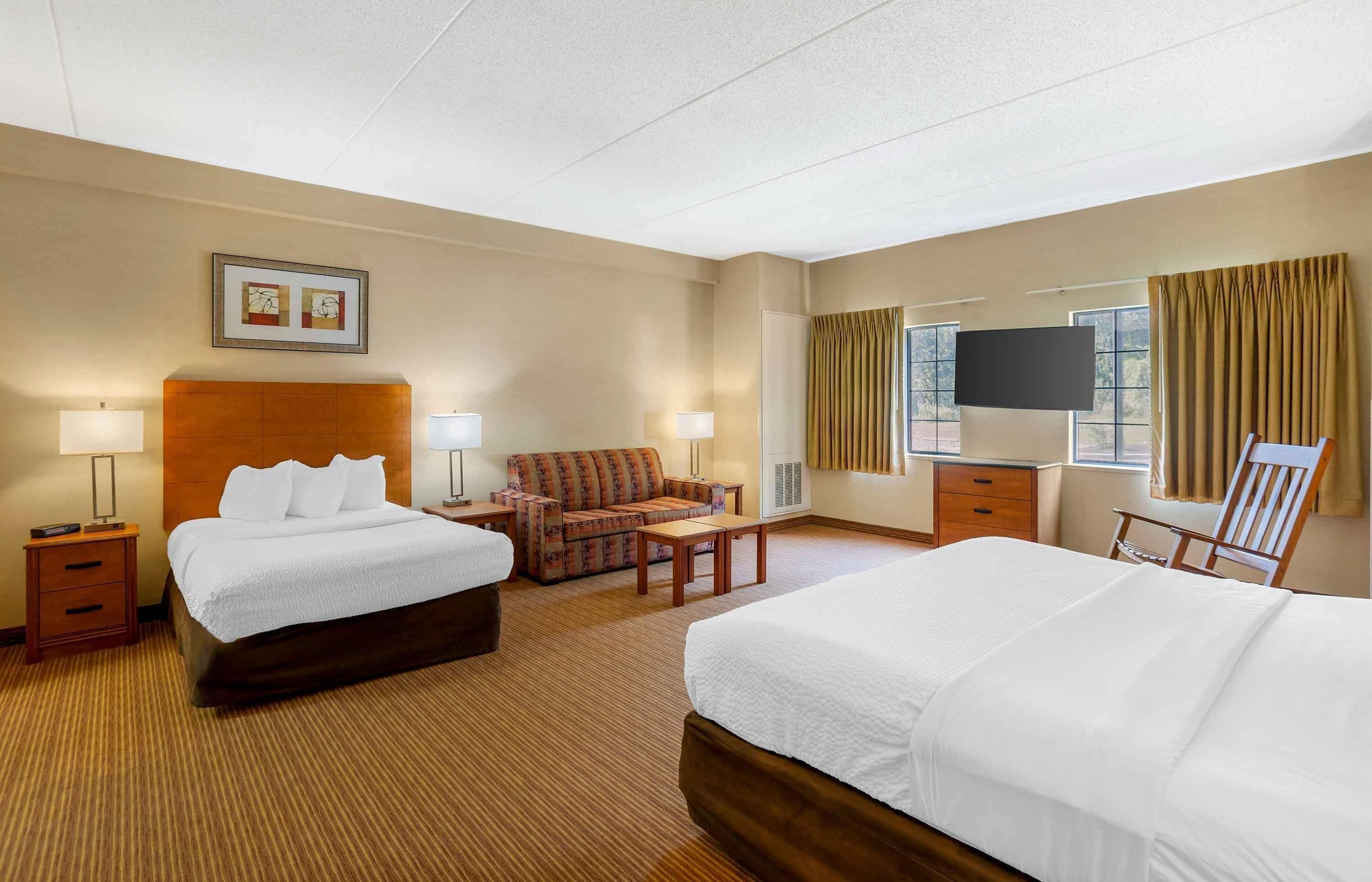 A hotel room with two beds, a sofa, a TV, and a window with curtains.