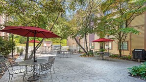 An outdoor patio area with hexagonal stone flooring, metal chairs, and red umbrellas. - Extended Stay America Suites Lancaster County (Mountville)