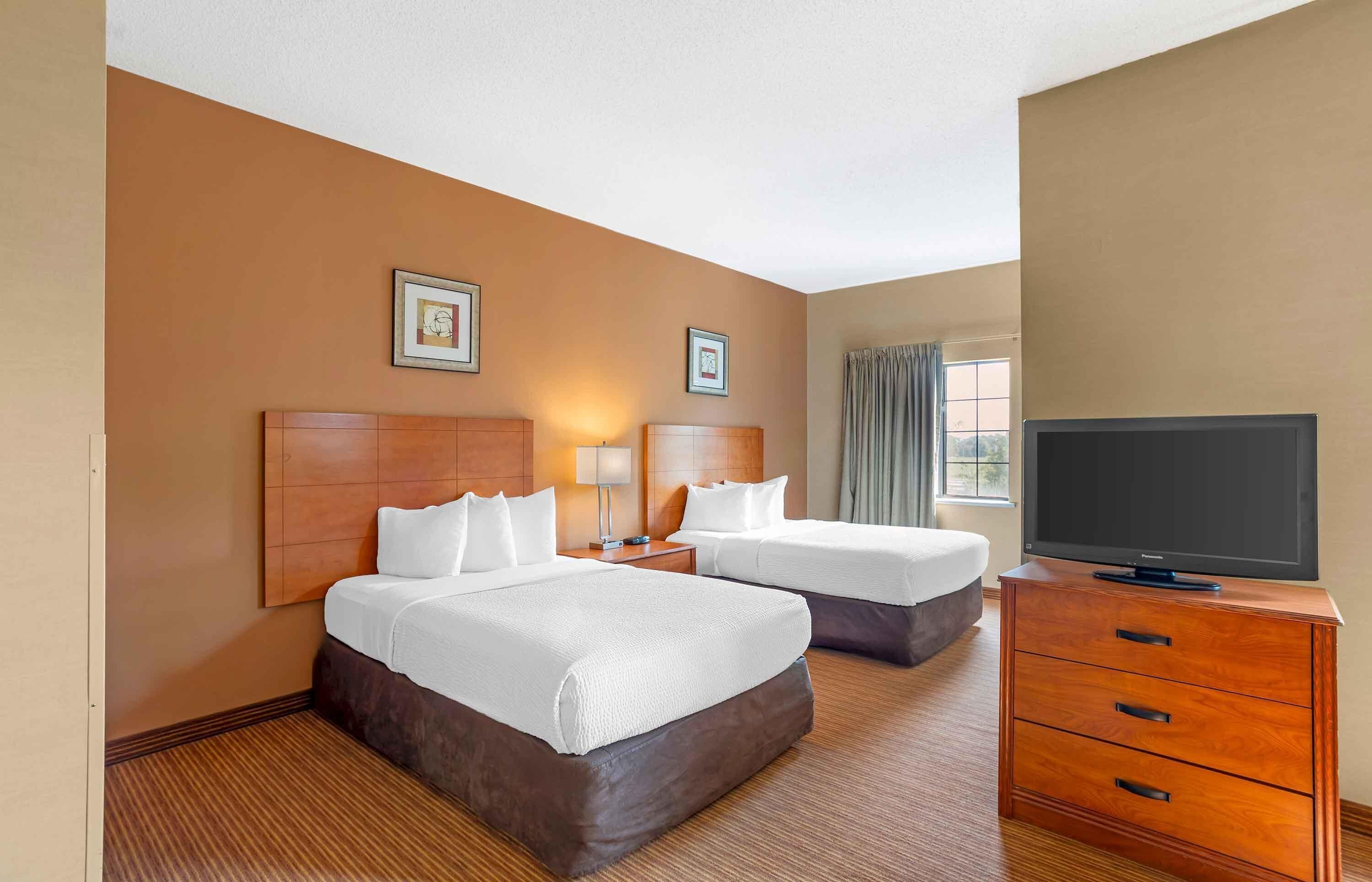 A hotel room with two beds, a TV, a dresser, and a window with curtains.