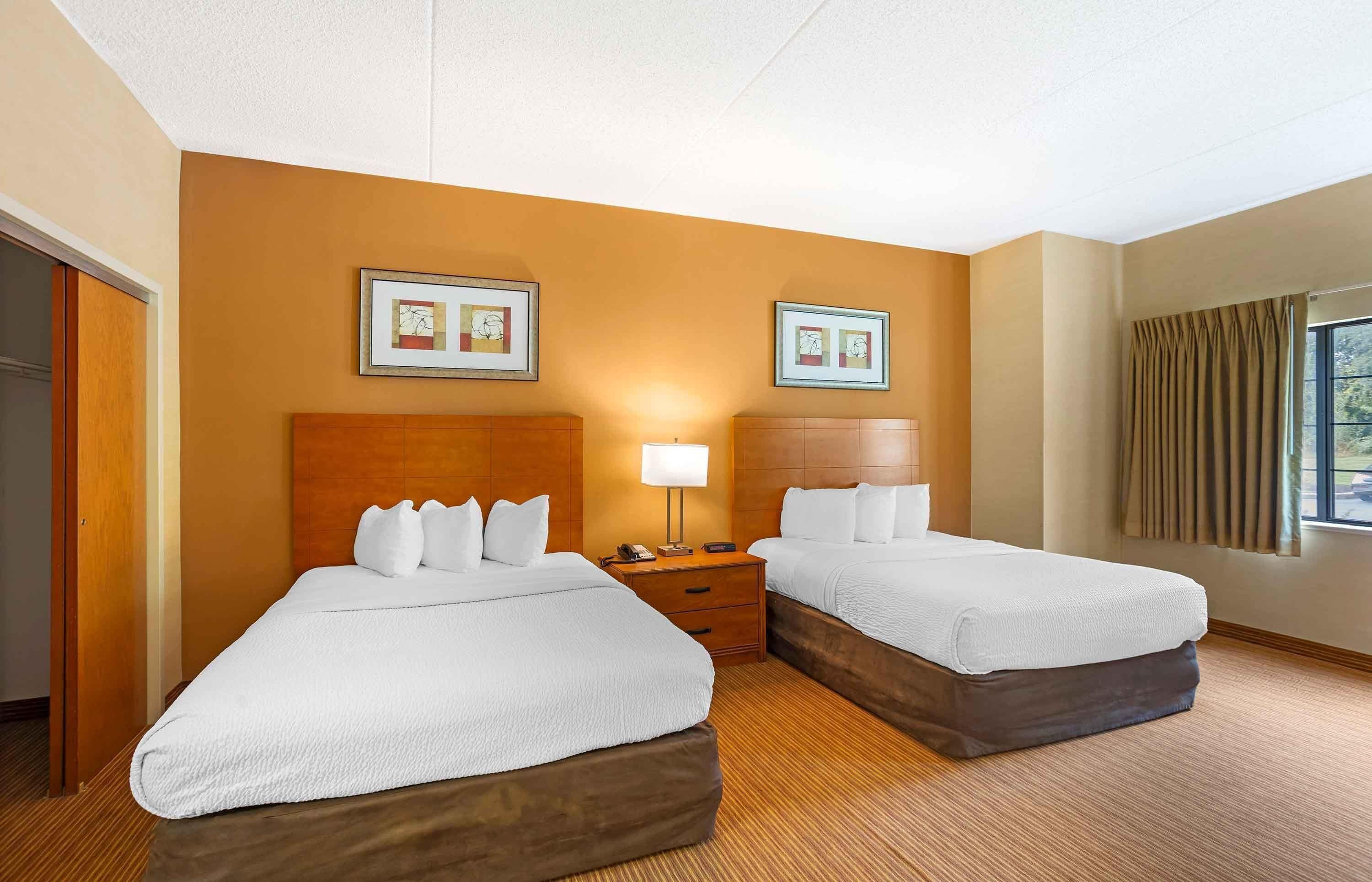 A hotel room with two beds, a wooden headboard, a nightstand with a lamp, and framed artwork on the wall.