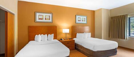 A hotel room with two beds, a wooden headboard, a nightstand with a lamp, and framed artwork on the wall.