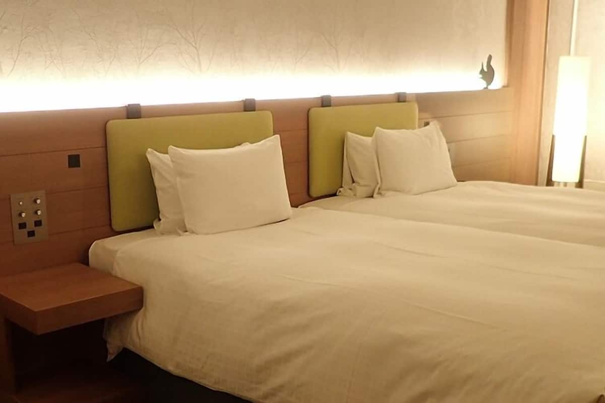 A hotel room with a large bed, two pillows, a nightstand, and a wall-mounted light fixture.