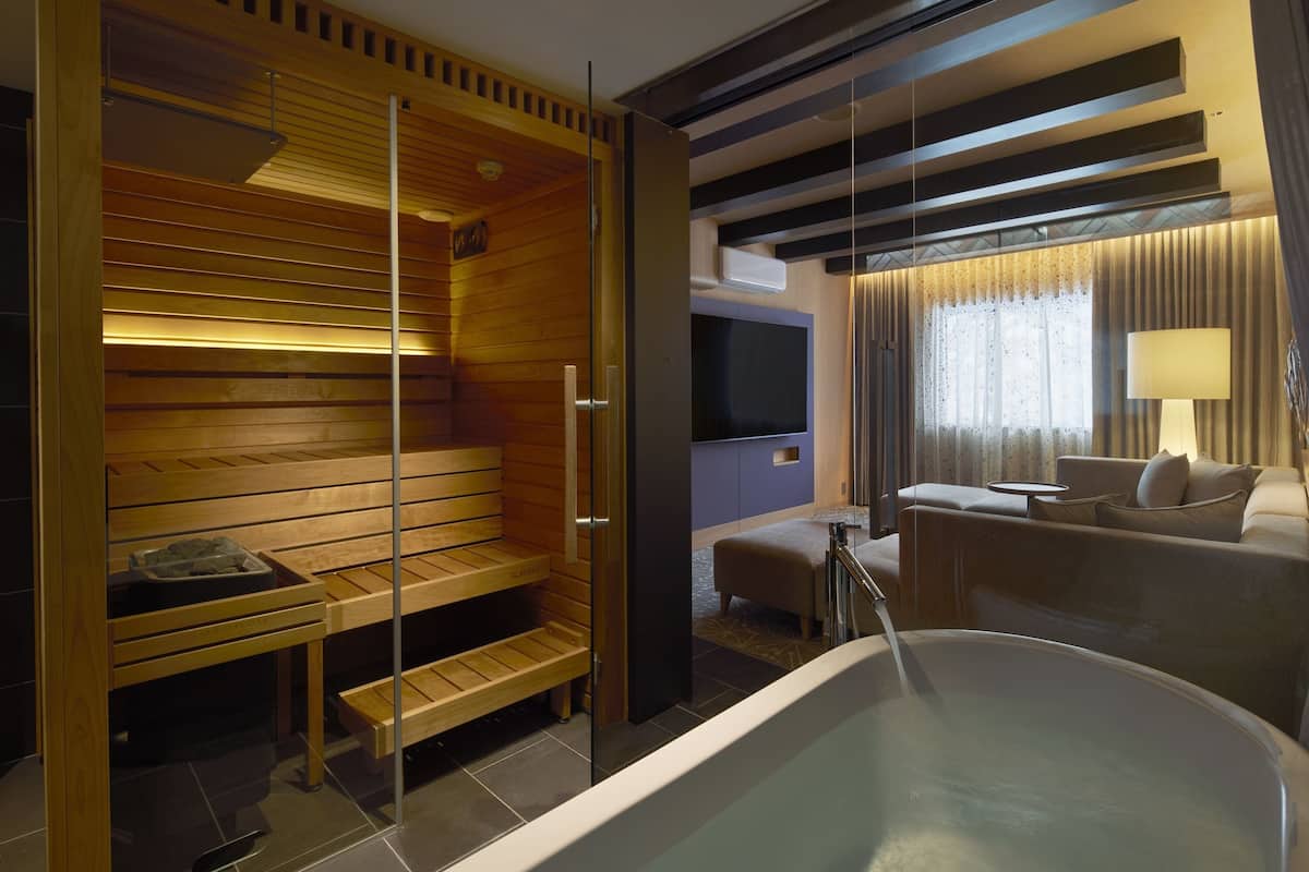 A modern spa room with a sauna, a large bathtub, a sofa, and a television.