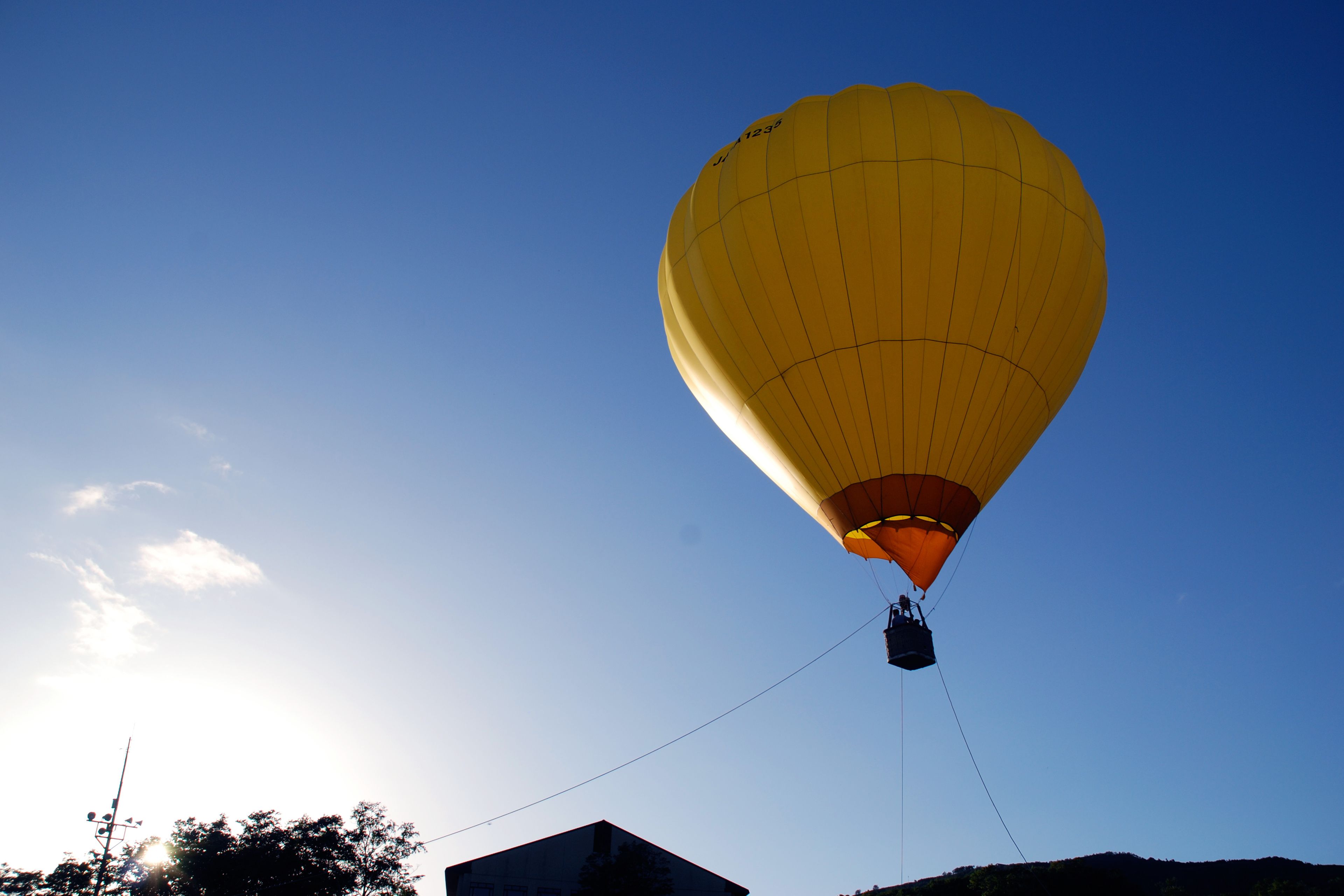 Un globo aerostático con una persona en la canasta, atado al suelo, frente a un cielo despejado.