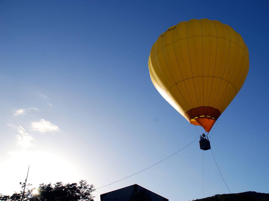 En varmluftsballong med en person i korgen, fastbunden i marken, mot en klar himmel.