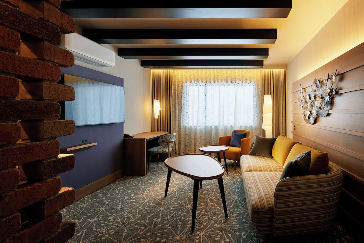 A modern hotel room with a brick wall, a sofa, a small table, and a desk.