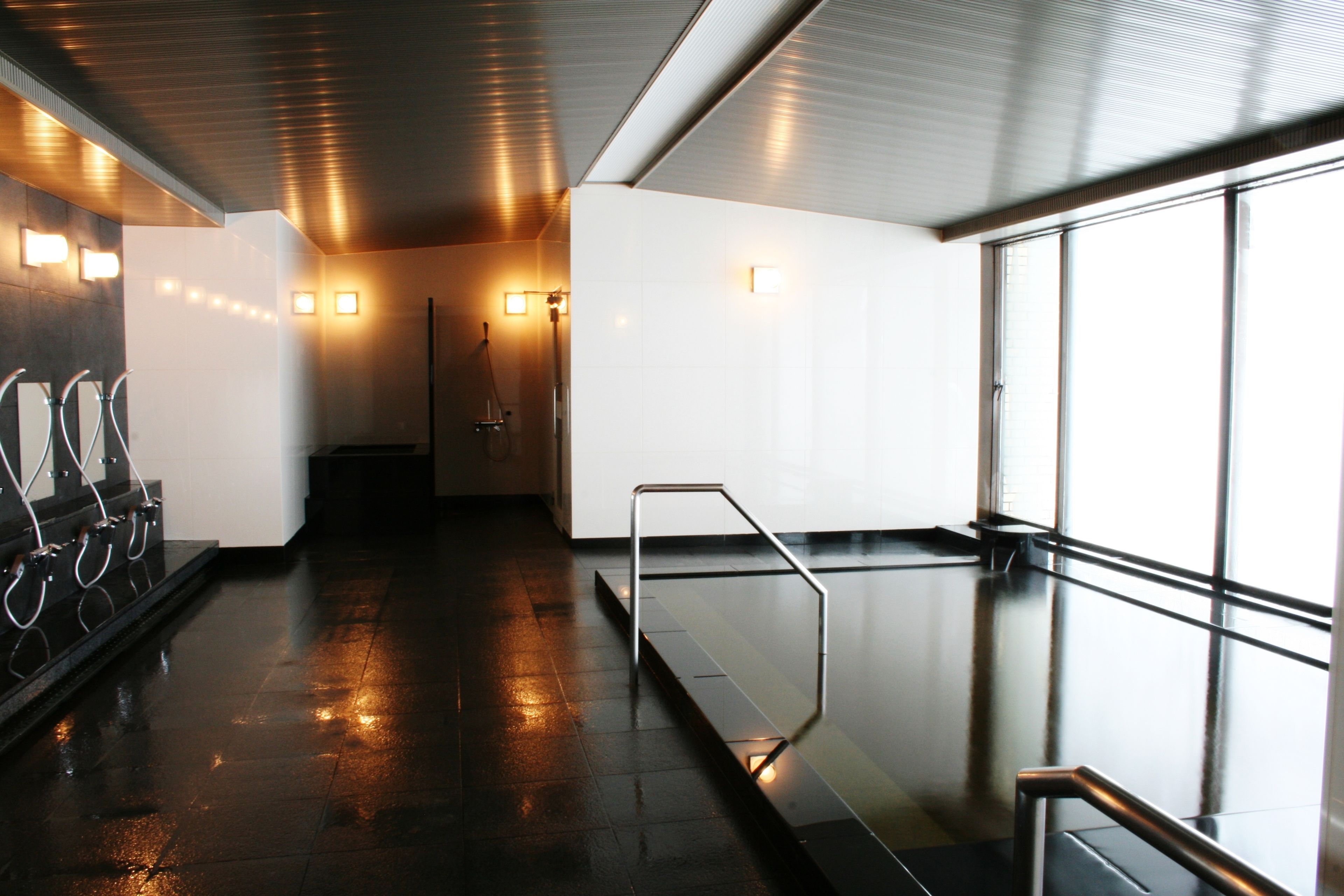 A modern indoor area with a wet floor, metal handrails, and a glass partition.