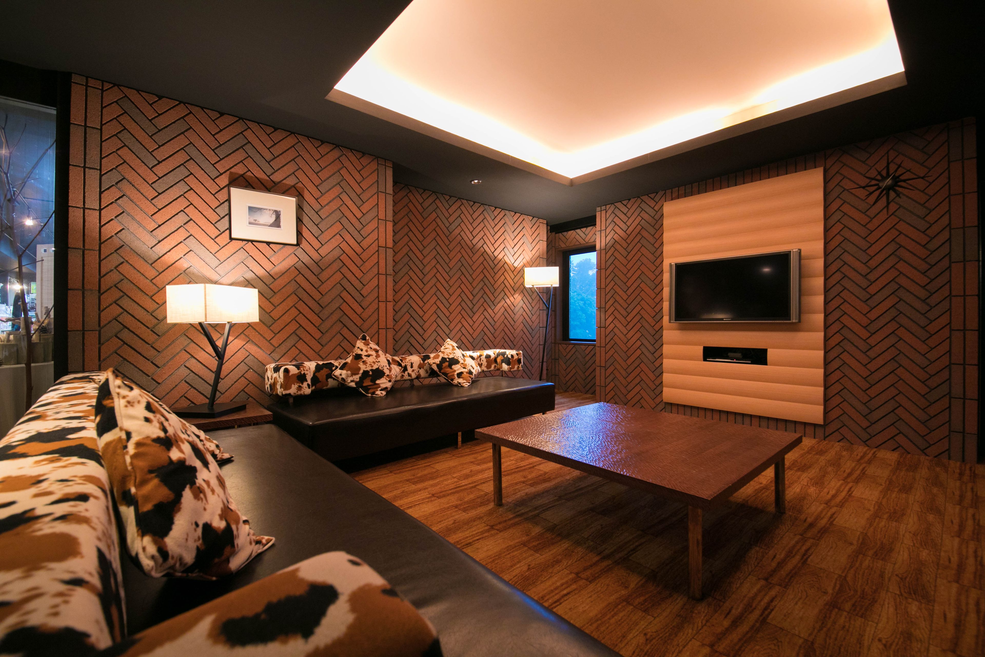 Una sala de estar moderna con un revestimiento de pared con motivo de espiga, un televisor de pantalla plana montado en un panel de madera, un sofá de cuero con cojines estampados y una mesa de centro de madera.