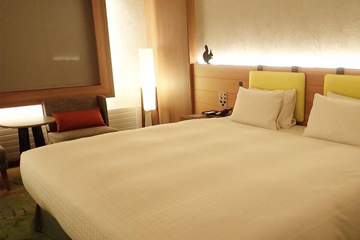 A hotel room with a large bed, a nightstand, a lamp, and a wall-mounted shelf with a decorative item.