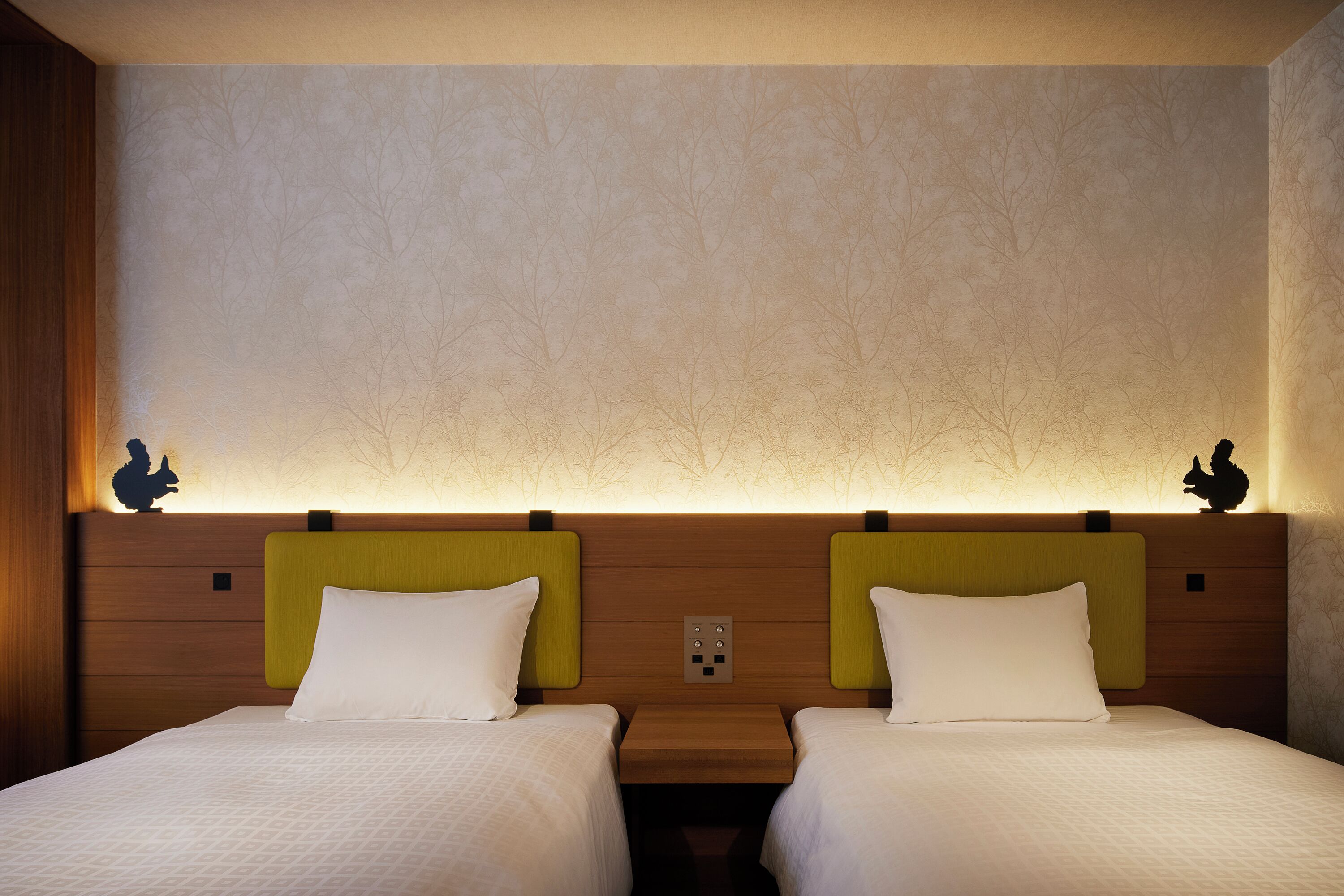Hotellihuone, jossa on kaksi erillistä sänkyä, puinen pääty ja seinä, jossa on puukuvioprintti.