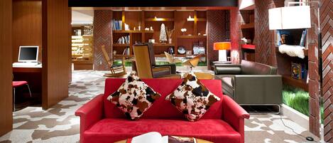 A modern living room with a red sofa, two patterned pillows, a coffee table with an open magazine, and a bookshelf in the background.