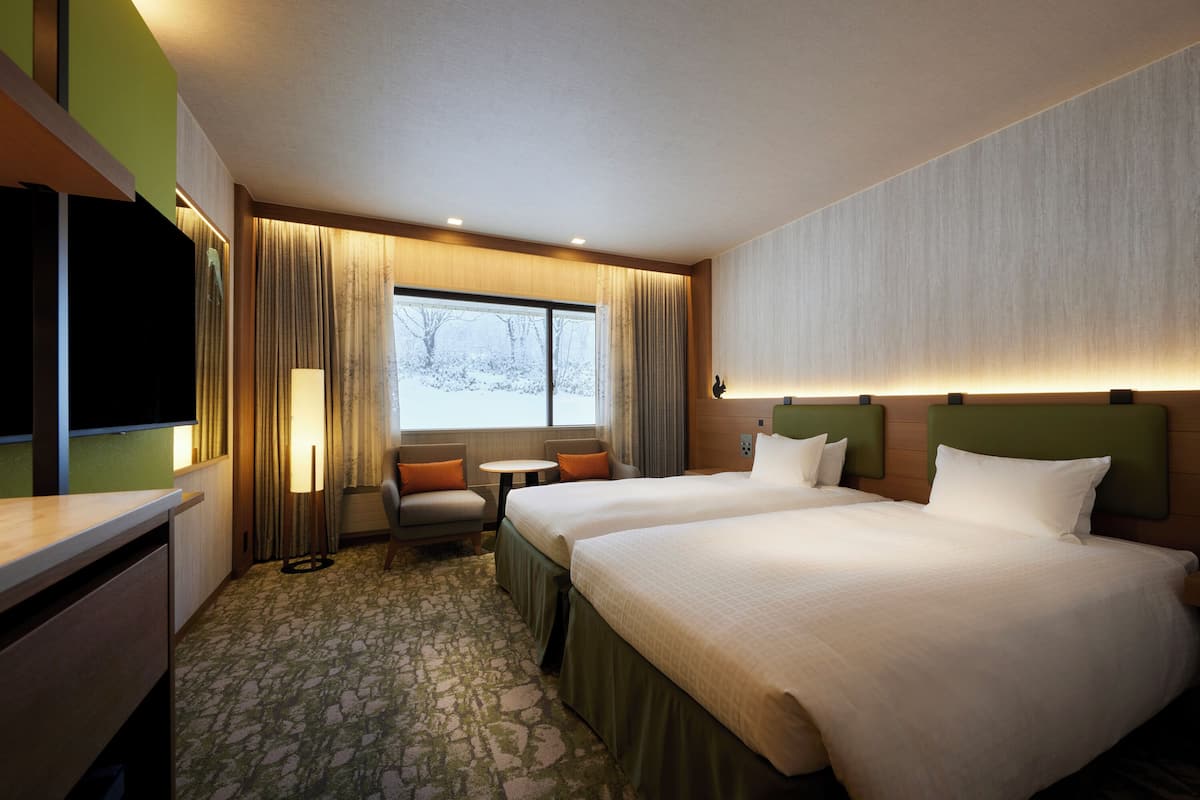 A hotel room with two beds, a desk, a chair, a small table, and a window with curtains.