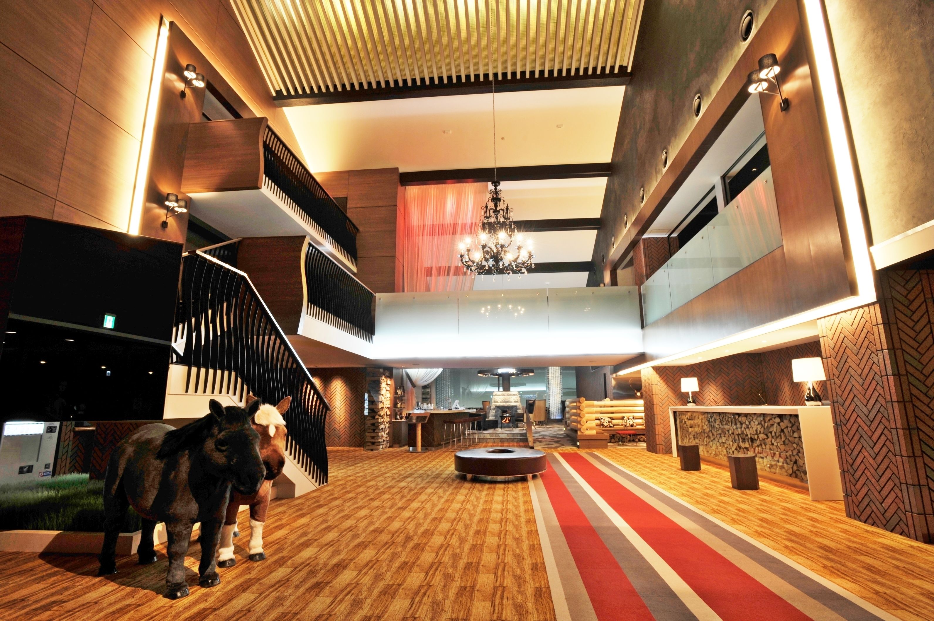 A spacious lobby with a wooden floor, a reception desk, a chandelier, and a staircase.