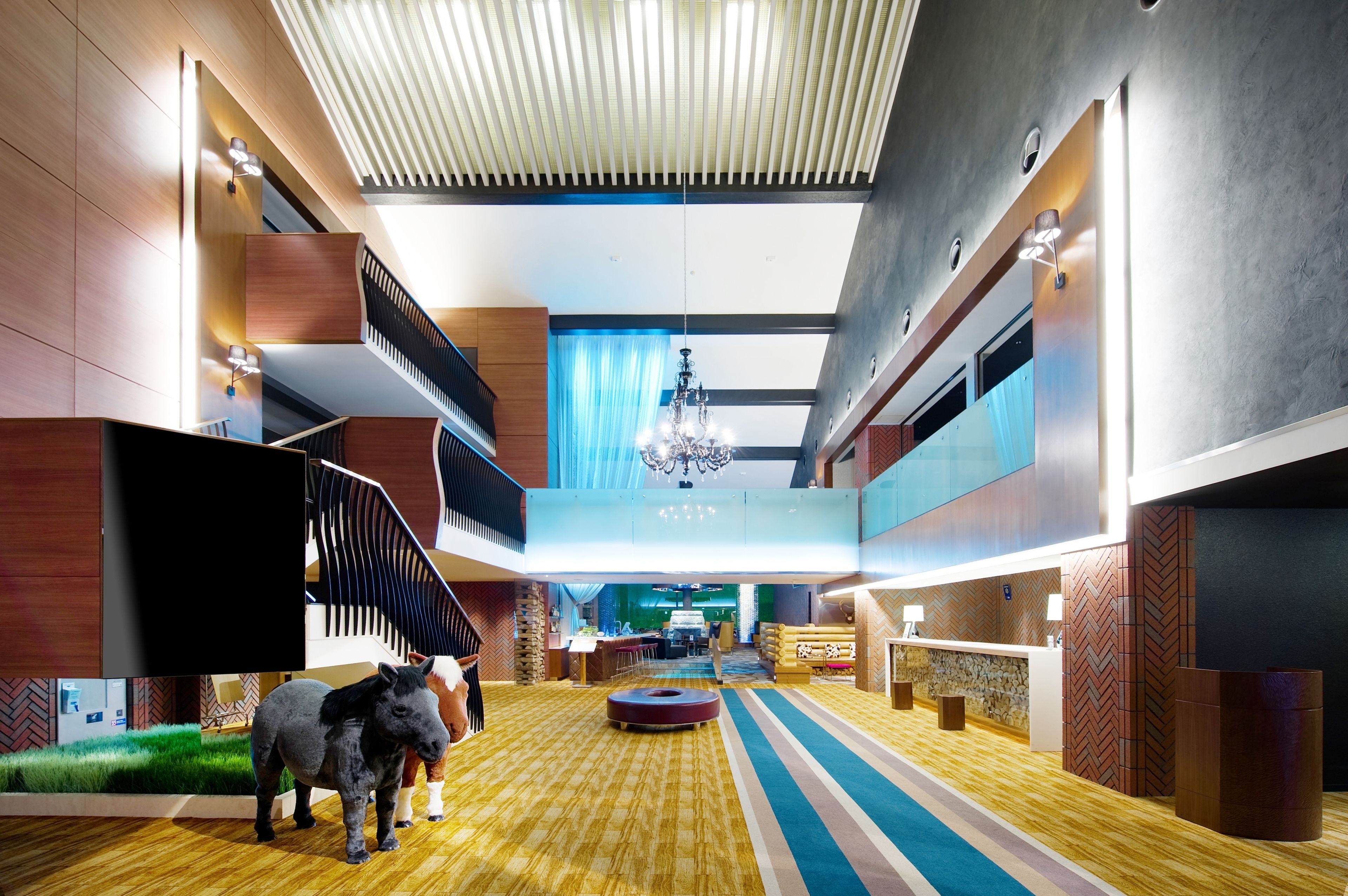 A modern hotel lobby with a central staircase, a chandelier, and a reception desk.