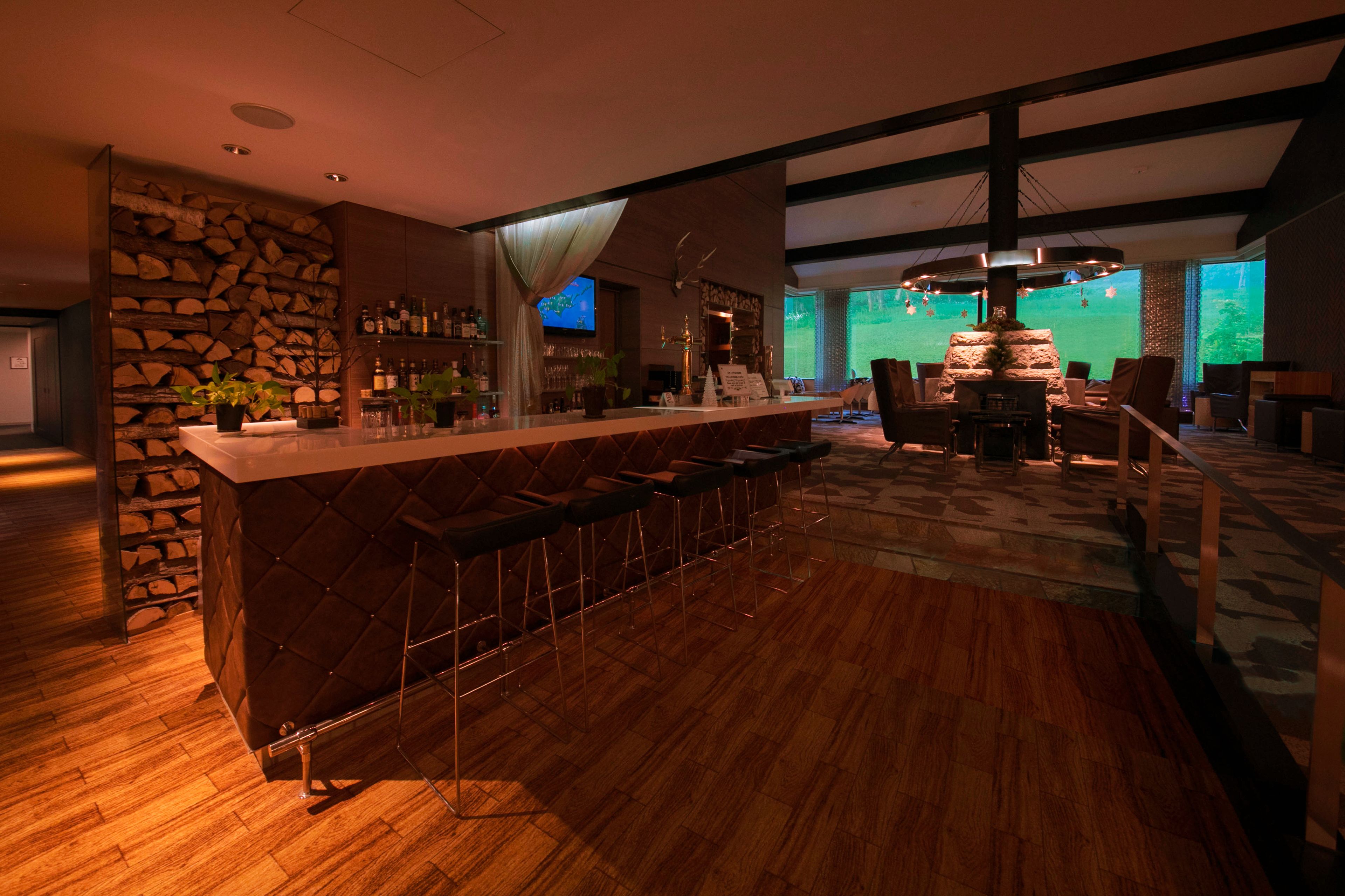 A modern bar area with a stone wall, bar stools, and a wooden floor.