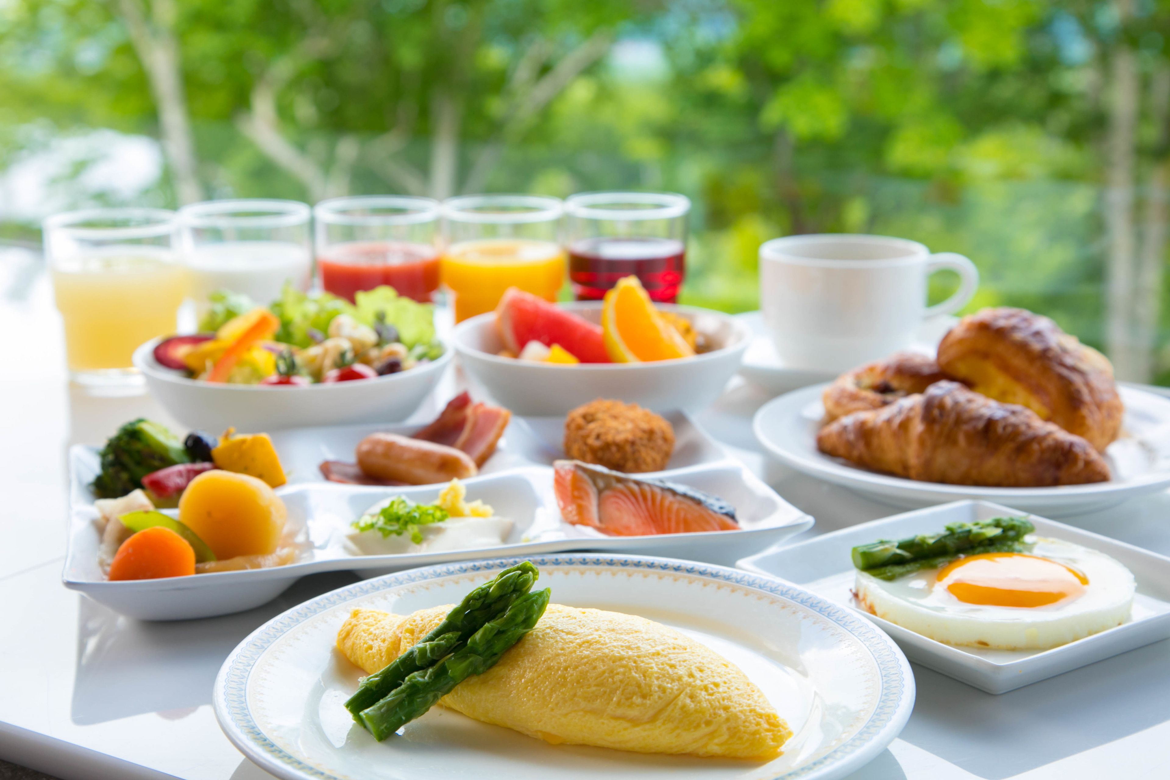 A breakfast tray with eggs, asparagus, croissants, and various fruits and juices.