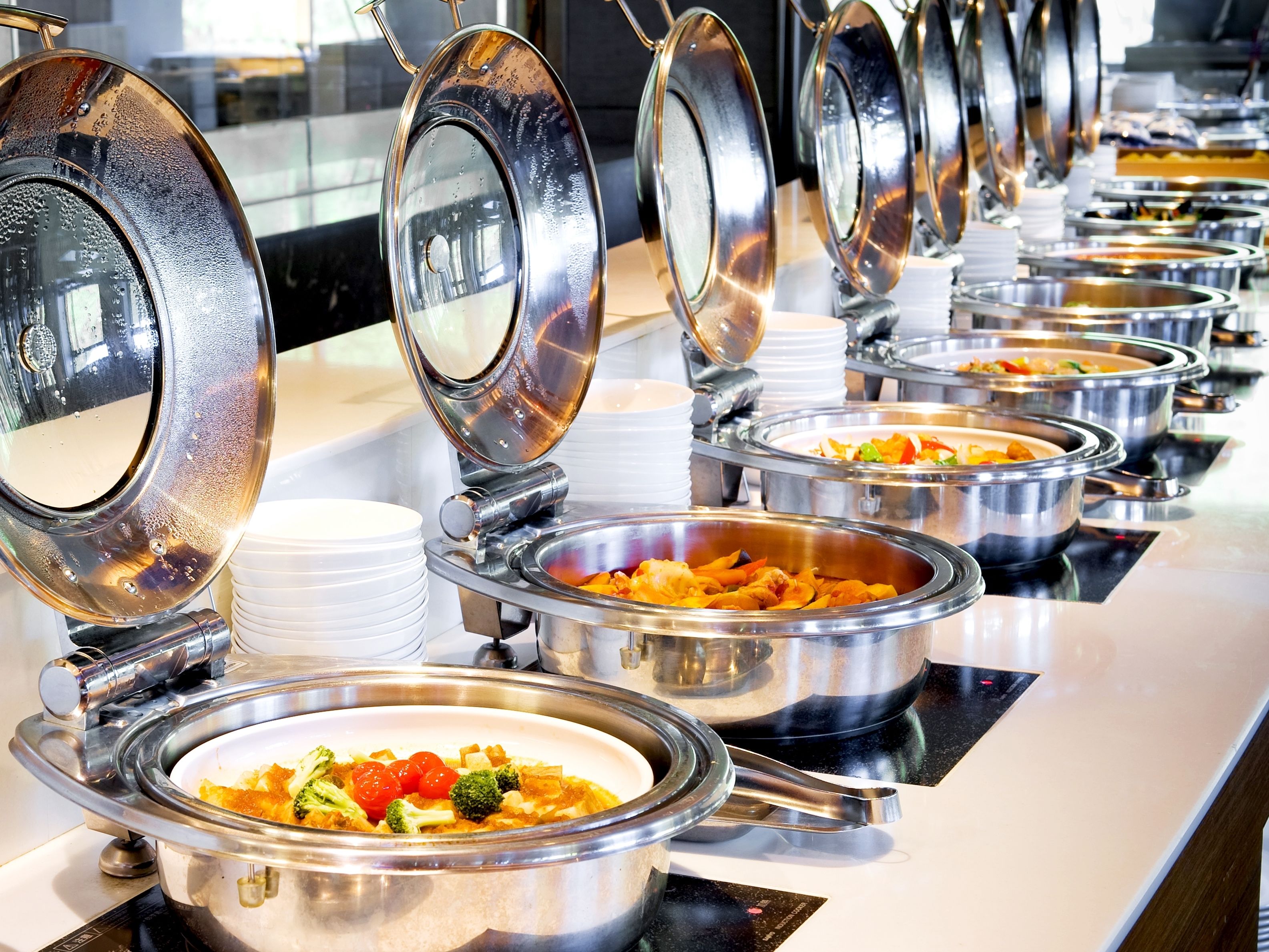 A buffet line with multiple stainless steel serving dishes, each with a lid.