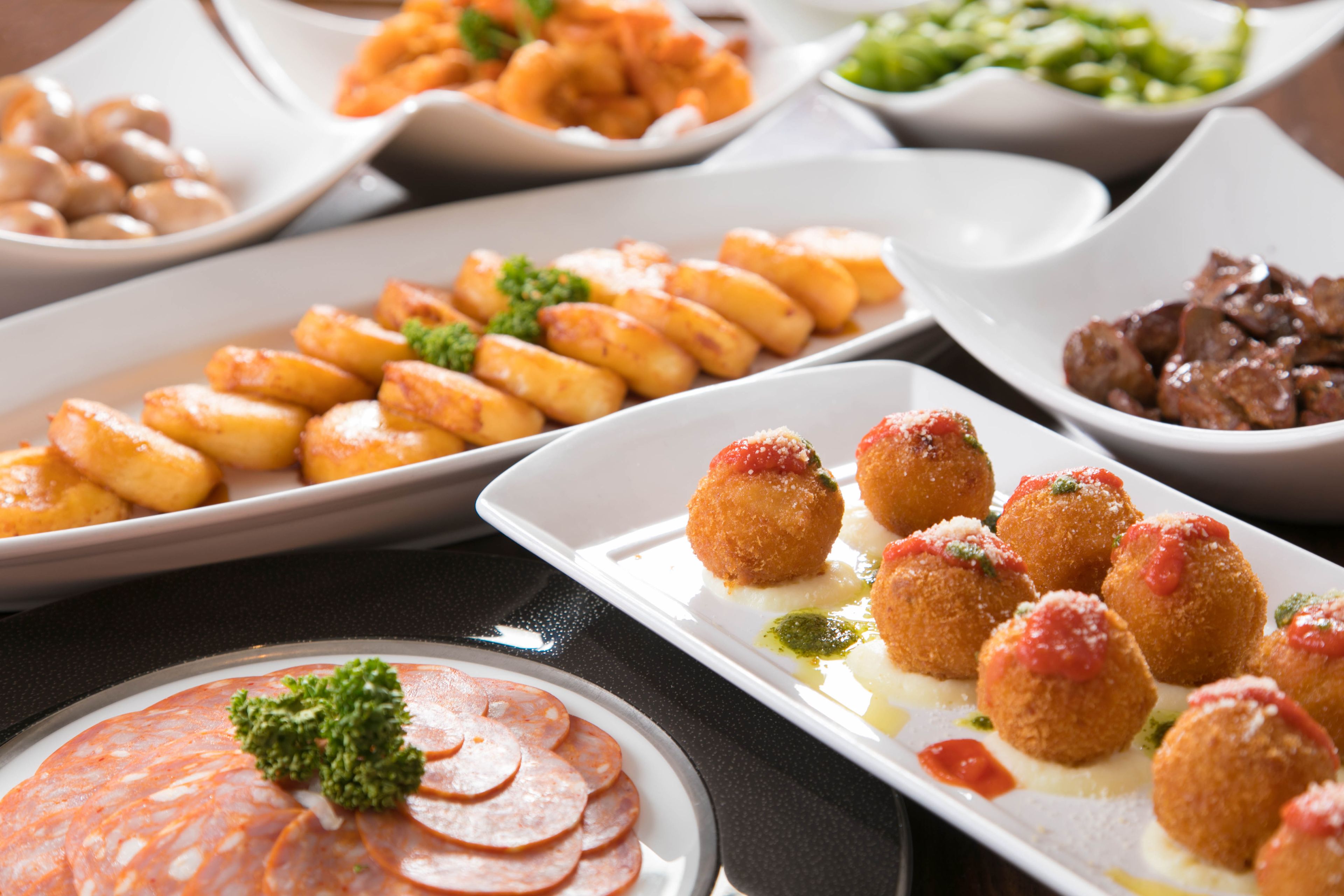 A variety of dishes including fried potatoes, meatballs, and a plate of sliced sausage.