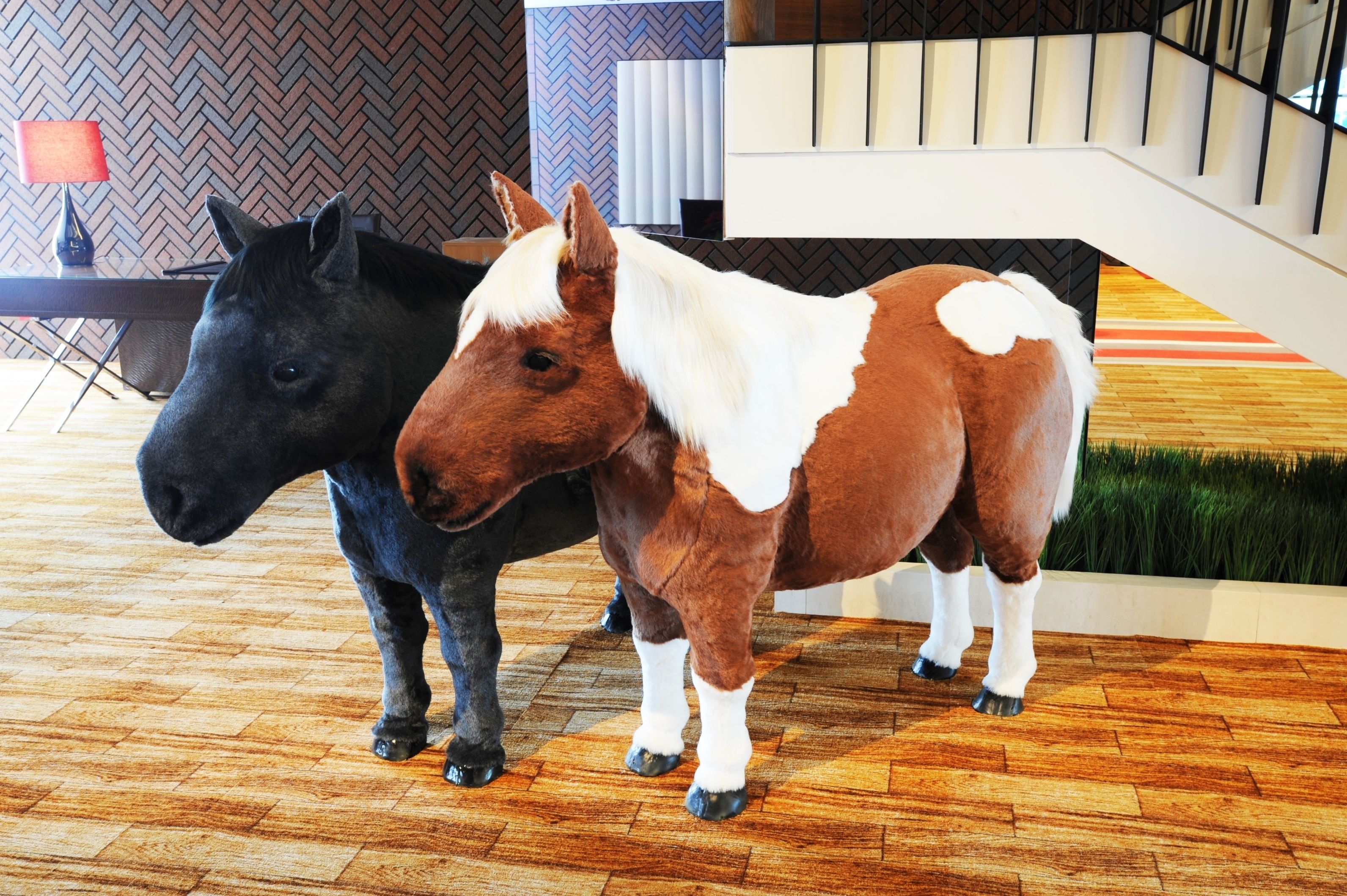 Two horse statues in a lobby with a herringbone floor pattern, a staircase, and a modern interior design.