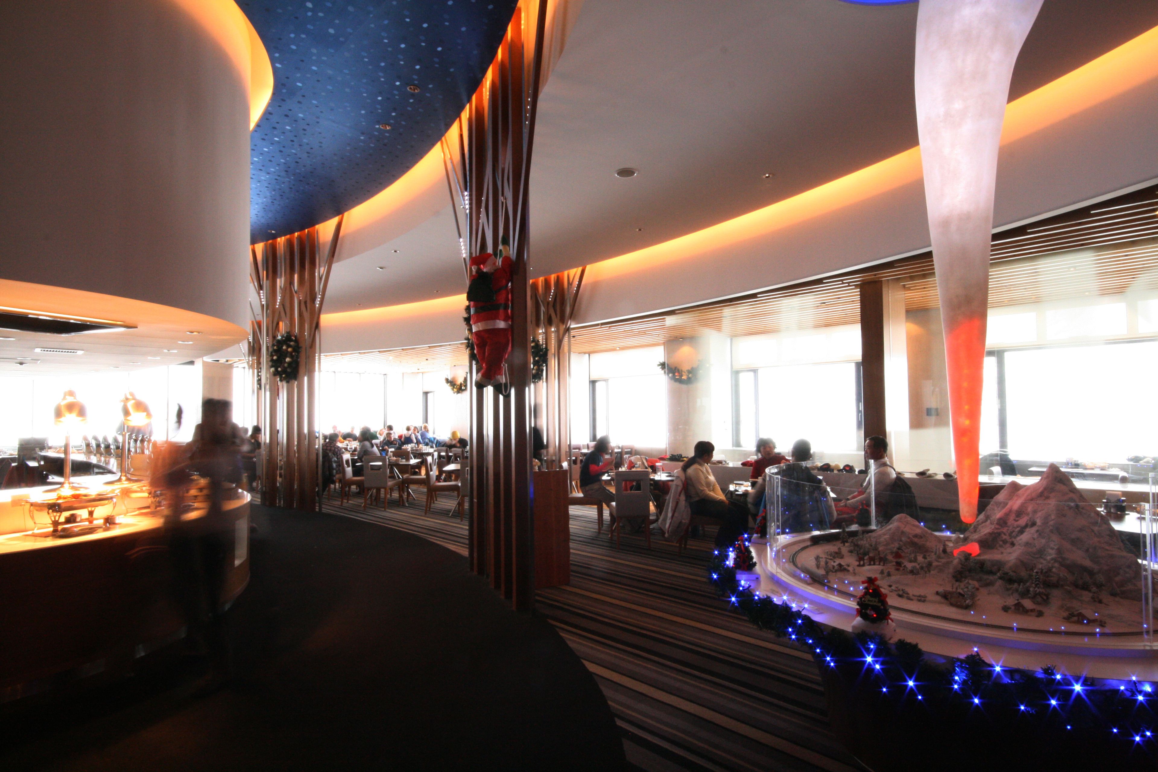 A modern restaurant with a central dining area, a bar, and a decorative model landscape.