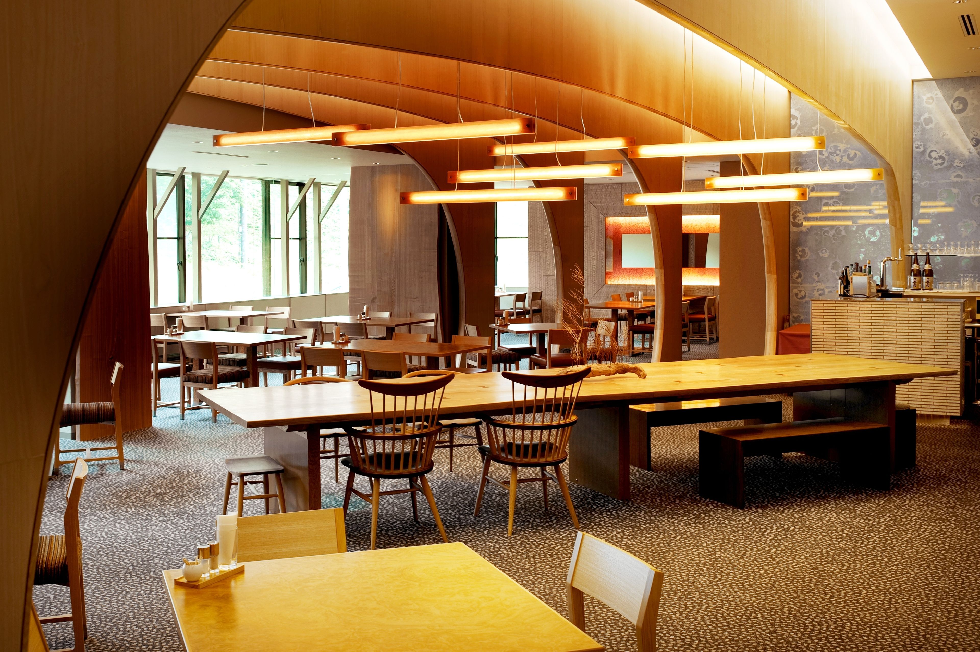 A modern library with wooden tables and chairs, large windows, and a curved ceiling.