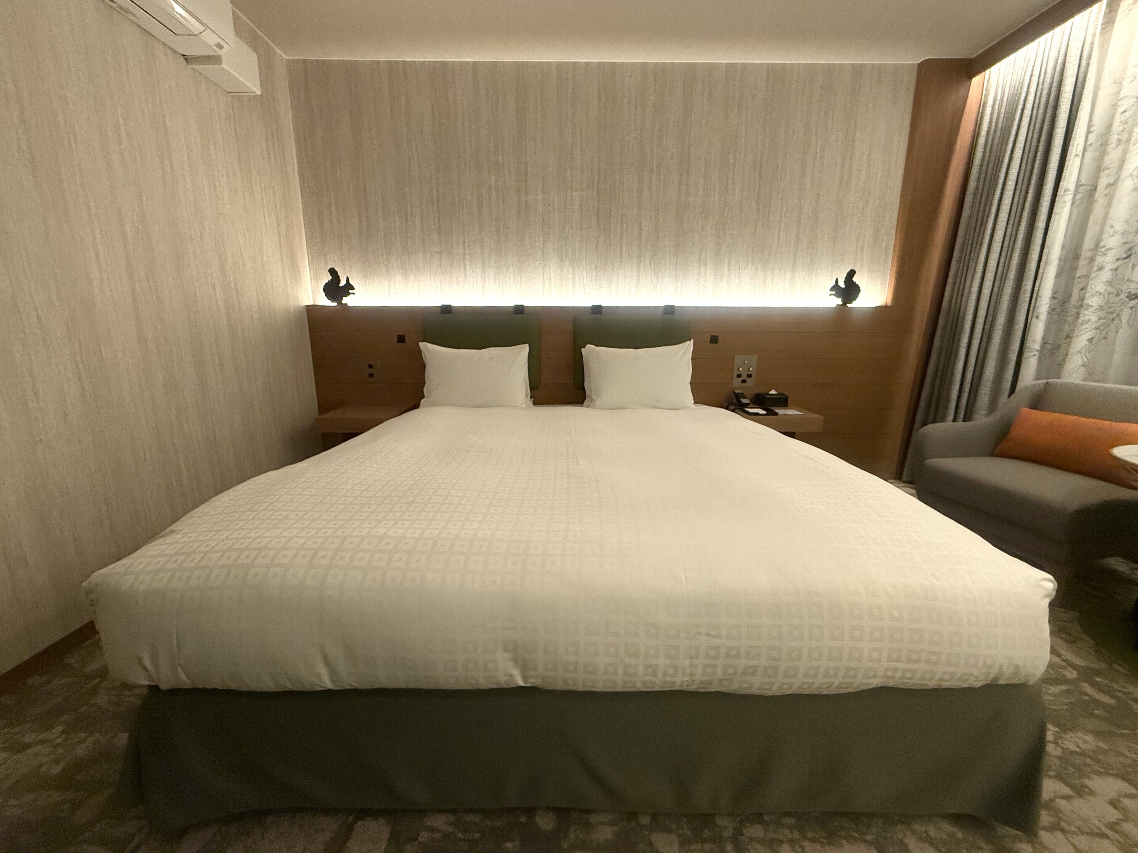 A hotel room with a large bed, a nightstand, a sofa, and a window with curtains.