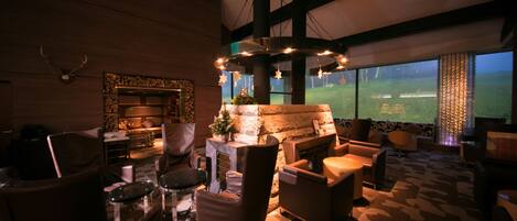 A spacious lounge area with a fireplace, comfortable seating, and a large window offering a view of the outdoors.