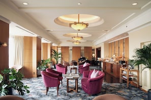 A hotel lobby with a reception desk, seating area with chairs, and a coffee station.