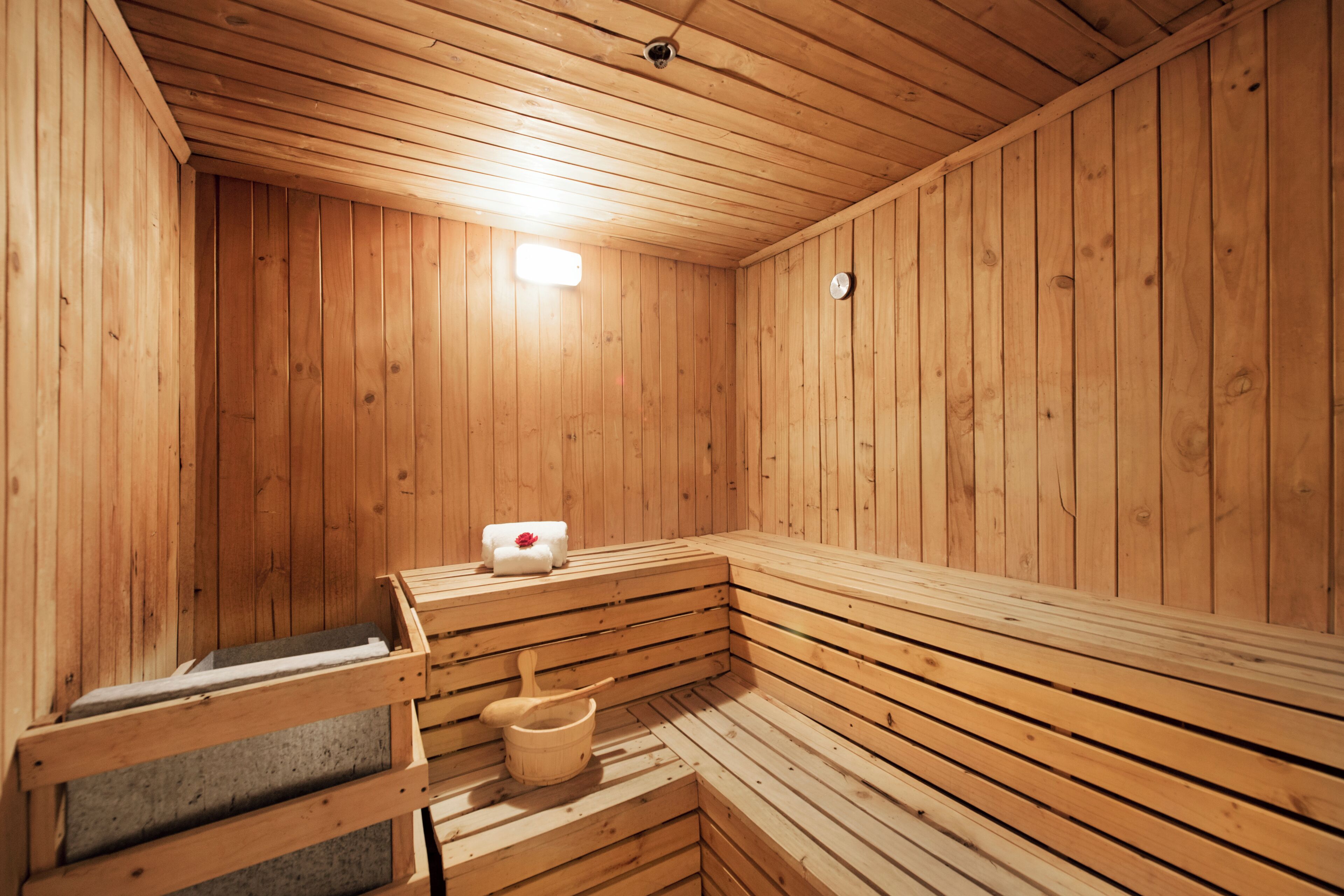 A wooden sauna with benches, a bench with a towel, and a wooden bucket.
