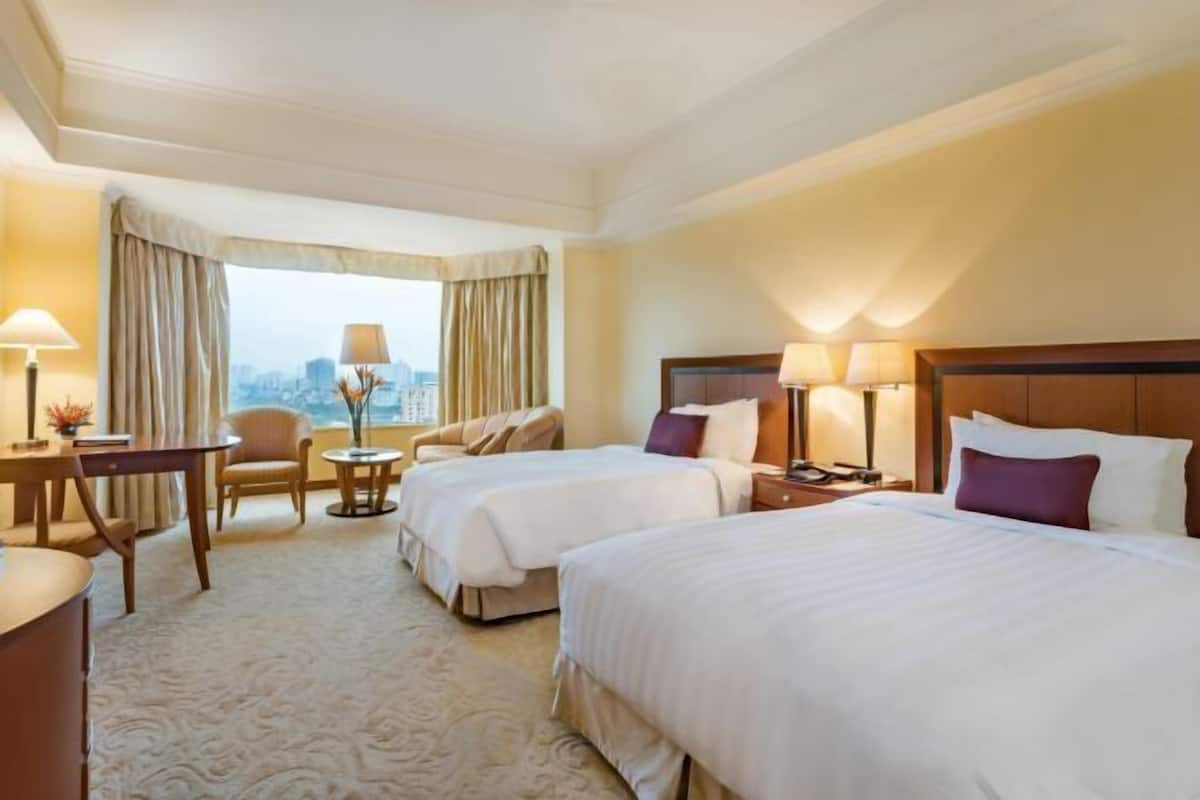 A hotel room with two beds, a desk, a chair, a small table, and a view of the city.