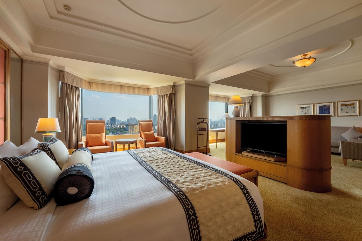 A hotel room with a large bed, a TV, a seating area with a view of the city, and a balcony.