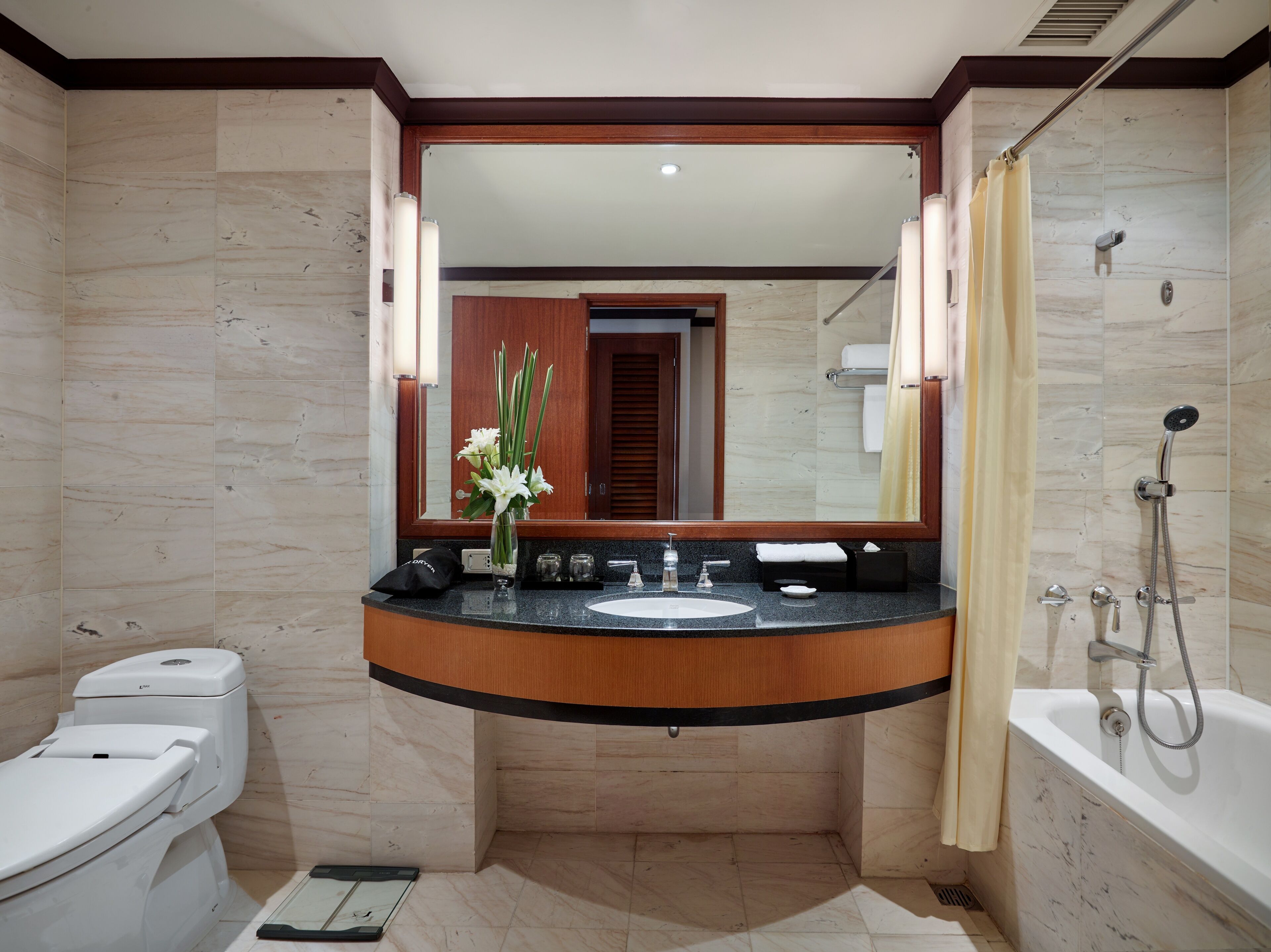 A modern bathroom with a marble floor, a white toilet, a sink with a wooden countertop, a large mirror, and a bathtub with a showerhead.