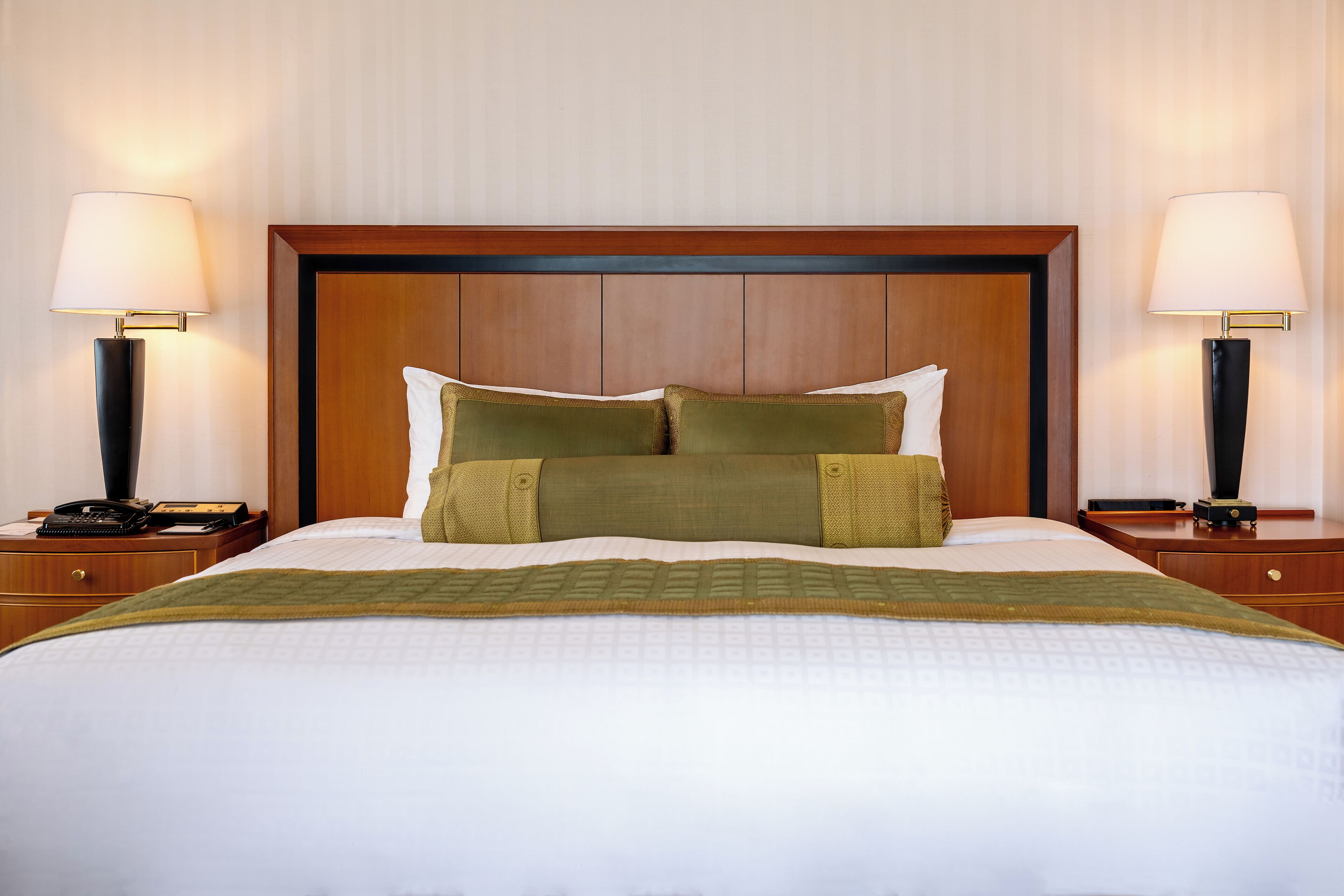A hotel room with a large bed, two bedside tables, a wooden headboard, and two lamps.