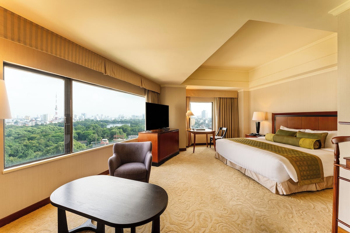 A hotel room with a large window, a bed, a desk, a chair, and a television.