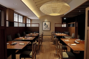 A restaurant interior with wooden tables, chairs, and a traditional Japanese calligraphy piece on the wall.