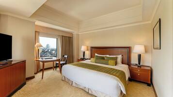 A hotel room with a large bed, two bedside tables with lamps, a desk with a chair, a television, and a window with a city view.