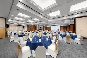 A conference room with multiple round tables, white chairs, and blue tablecloths.