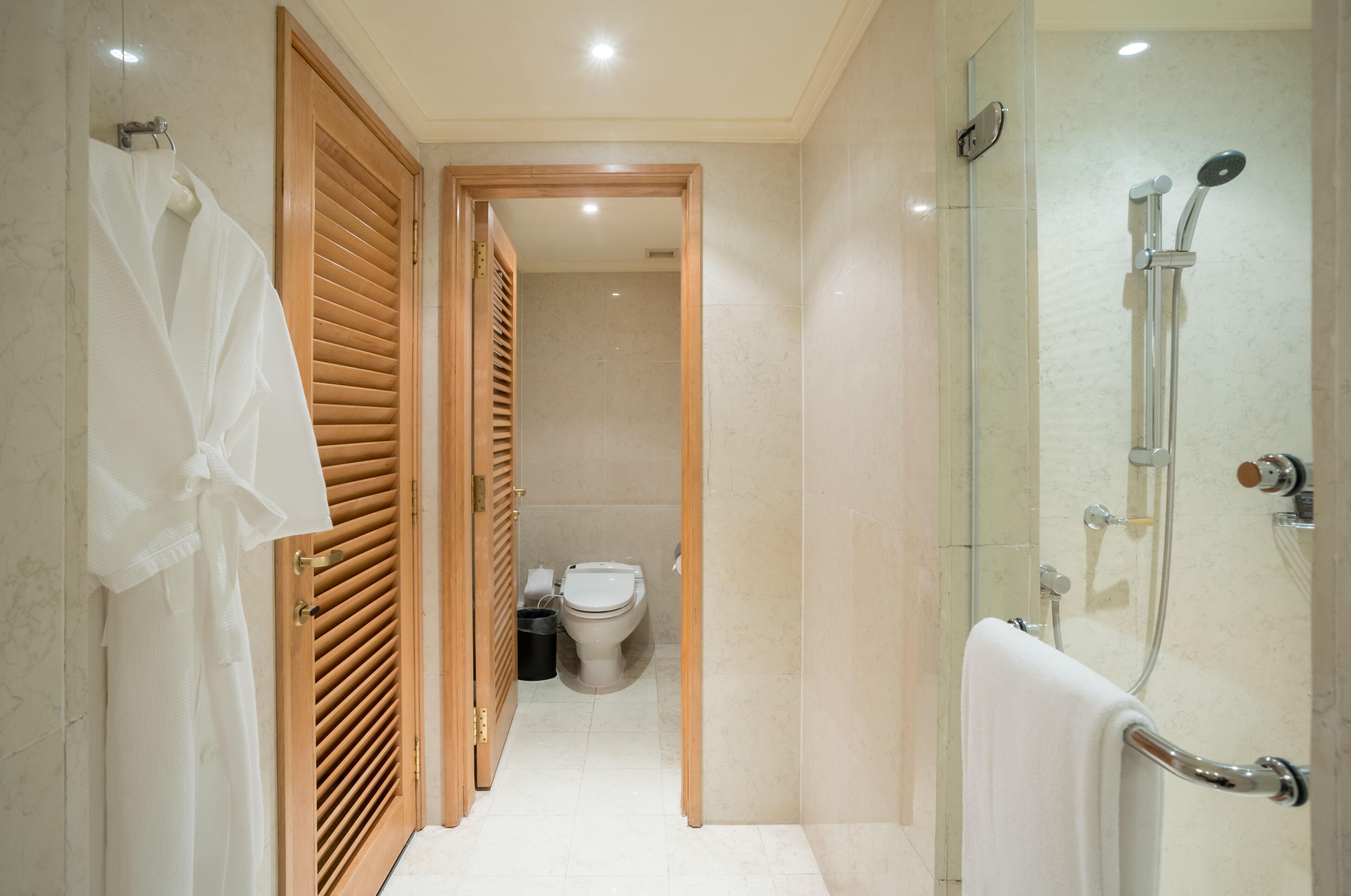 Un baño moderno con ducha de vidrio, puertas de madera y un inodoro a la vista en el fondo.