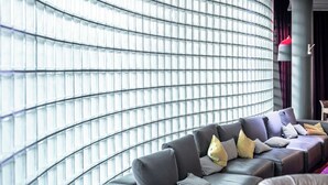 A modern living room with a curved glass wall, a dark leather sofa, and a red accent lamp. - pentahotel Kassel (Kassel)