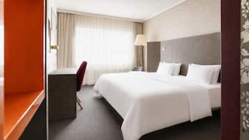A hotel room with a bed, a desk, a chair, a lamp, and a window with curtains.