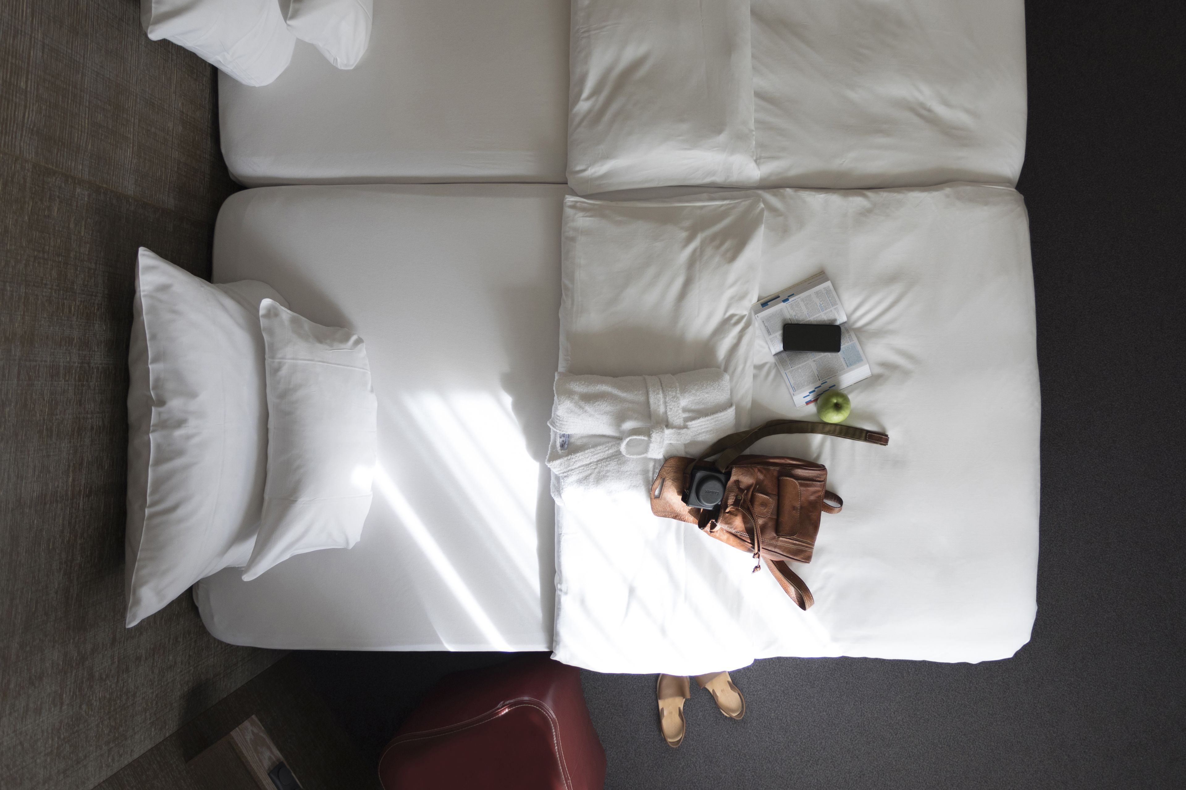Ein ordentlich bezogenes Bett mit weißen Leinen, eine braune Lederstasche und ein Smartphone darauf.