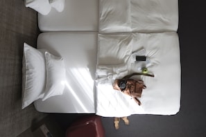 A neatly made bed with white linens, a brown leather bag, and a smartphone on the bed.