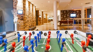 Une table de baby-foot dans le hall d’un hôtel, avec un mur en briques et une table de billard en arrière-plan.