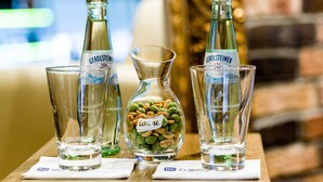 Trois bouteilles de bière Gerolsteiner, une carafe en verre et un verre contenant des amuse-gueules, le tout posé sur une table en bois.