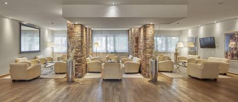 A spacious room with multiple seating areas, a large window, and a flat-screen TV on the wall.