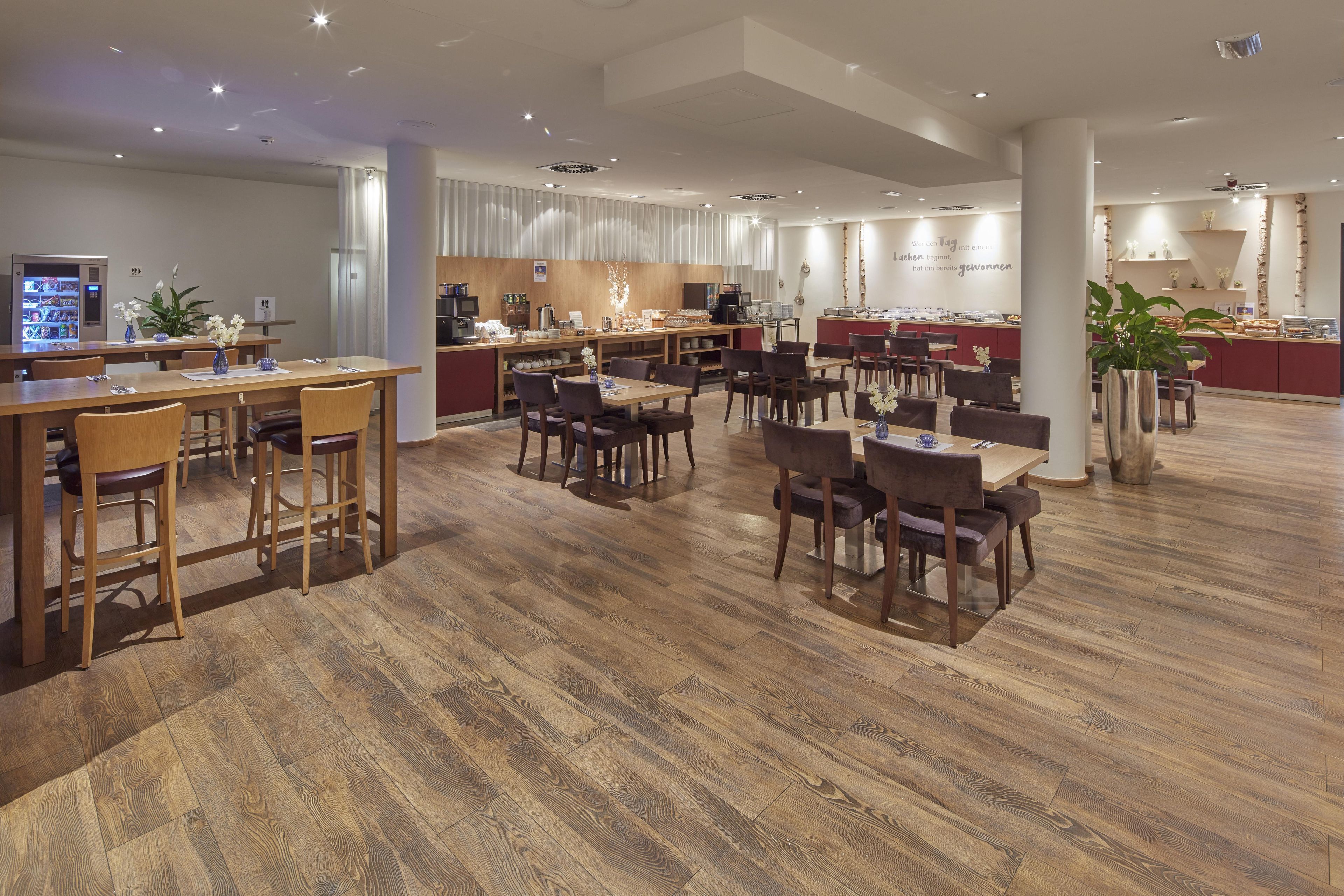 A spacious dining area with wooden flooring, multiple tables and chairs, a coffee machine, and a buffet counter.