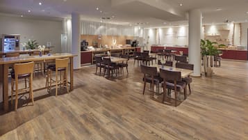 Un vaste espace dédié à la salle à manger, doté d’un plancher en bois, de plusieurs tables et chaises, d’une machine à café et d’un comptoir de buffet.