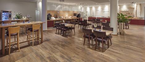 A spacious dining area with wooden flooring, multiple tables and chairs, a coffee machine, and a buffet counter.