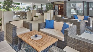 A modern lounge area with wicker furniture, a wooden table, and potted plants.
